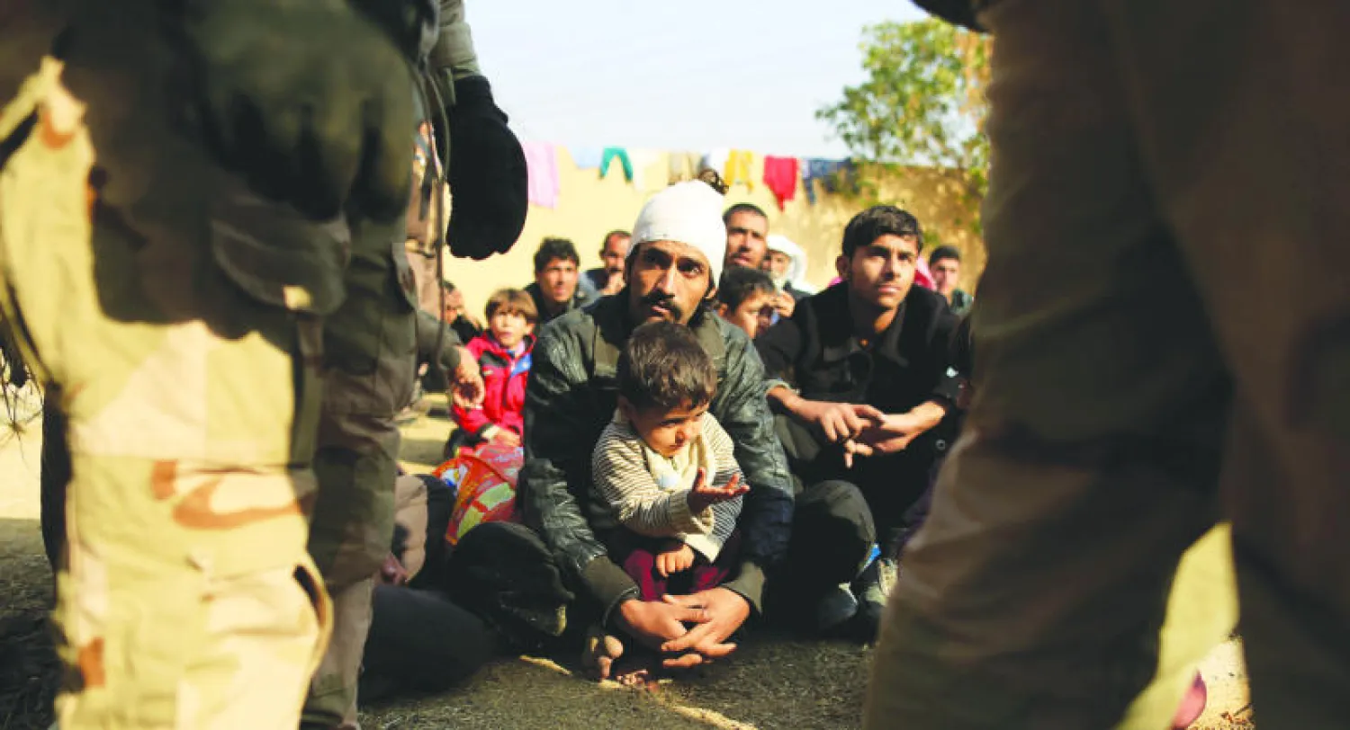 رجال نزحوا جراء المعارك بين القوات العراقية و«داعش» في حي الانتصار بالموصل ينتظرون التحقيق الأمني معهم أمس (رويترز)