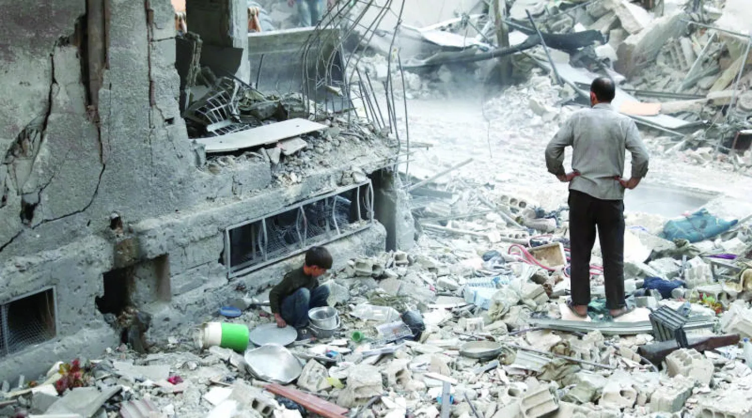 طفل سوري يبحث عن بعض المقتنيات بين حطام مبنى في بلدة دوما دمر بسبب قصف طائرات النظام (أ.ف.ب)