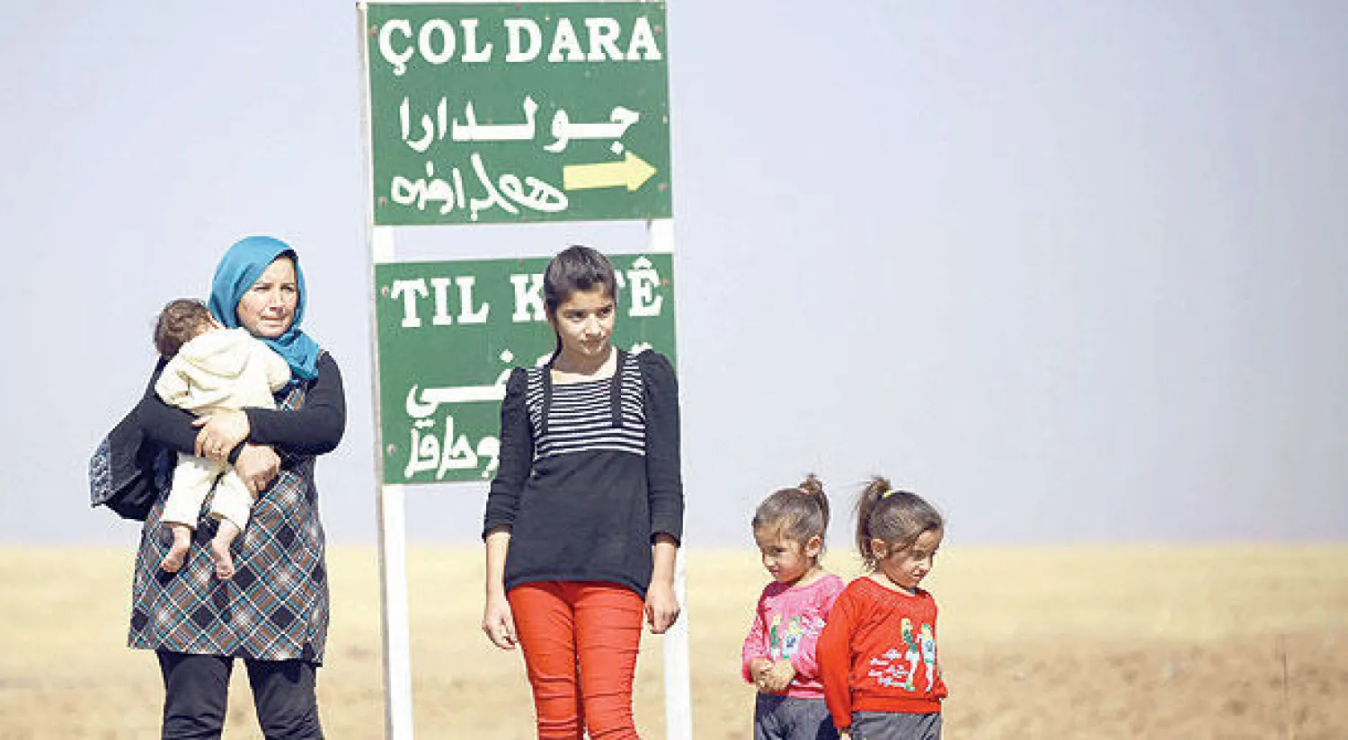 كردية مع أطفالها عند مدخل قرية الشجرة في مدينة القامشلي وهي جزء من مشروع طموح للأكراد في المنطقة (أ.ف.ب)