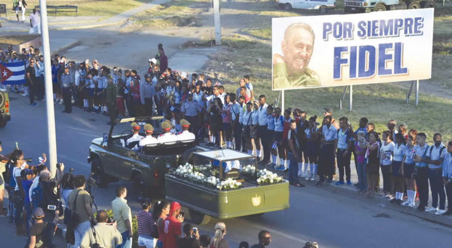كوبيون يودعون فيدل كاسترو خلال مرور موكب يحمل رماده إلى جانب لافتة «فيدل للأبد» بسانتياغو أمس (أ.ف.ب)