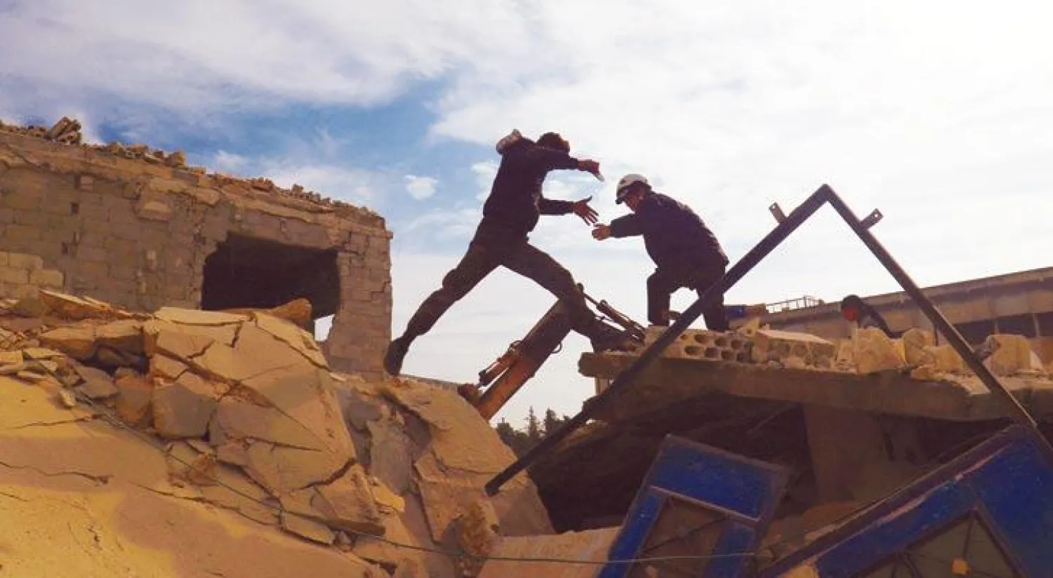 عنصر من الدفاع المدني في مدينة إدلب أمس يساعد أحد المدنيين على القفز فوق ركام مبنى تهدم بفعل غارات الطيران الروسي على المدينة وريفها في الفترة الأخيرة (رويترز)