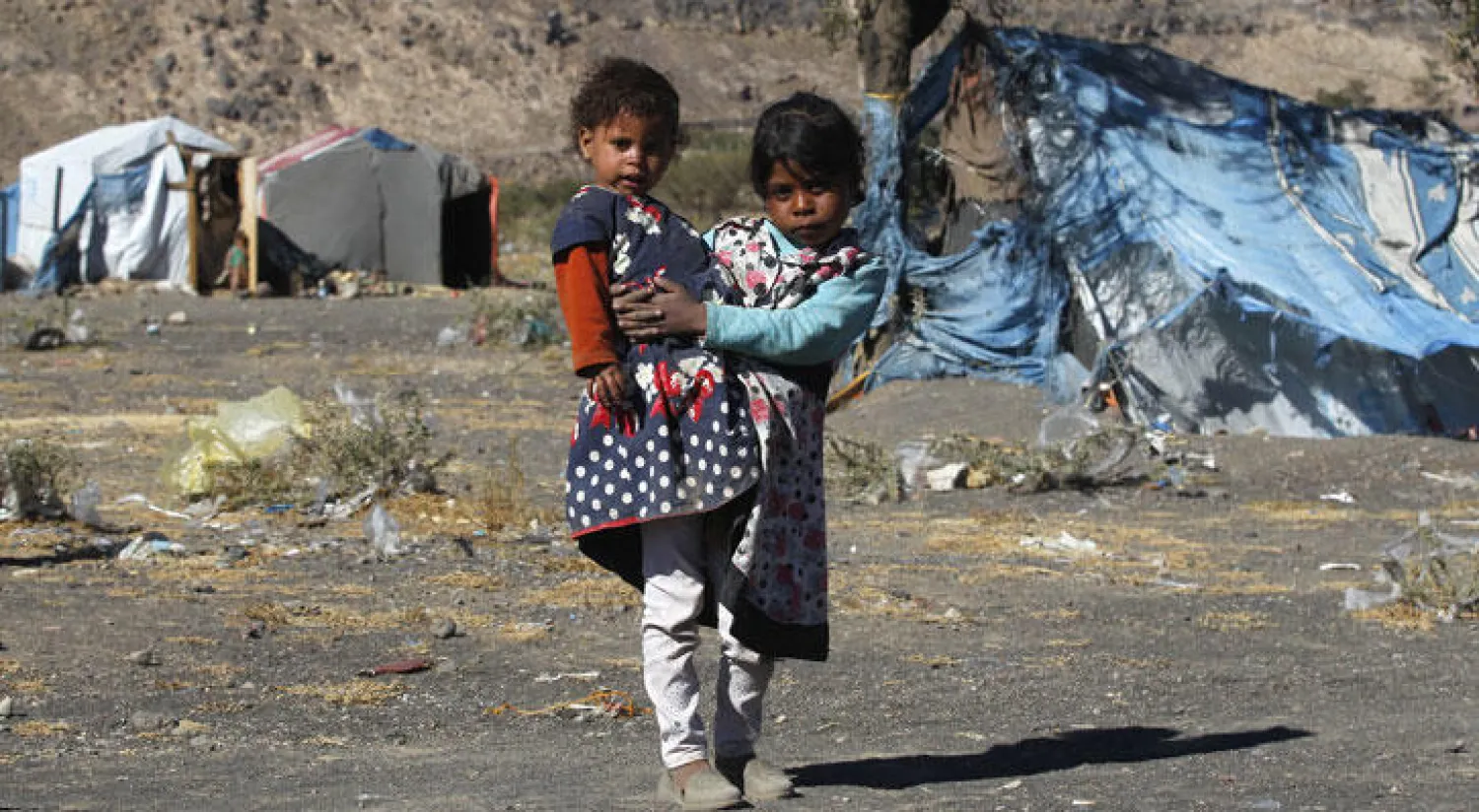 طفلة تحمل أختها في مخيم للنازحين في ضواحي صنعاء الأربعاء الماضي (إ.ب.أ)