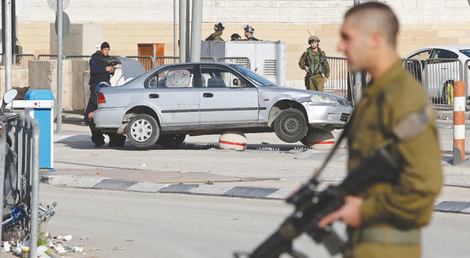 جنود الاحتلال يفتشون سيارة ادعوا أن سائقتها اندفعت بها نحو الحرس عند معبر قلنديا بين القدس ورام الله (أ.ف.ب)