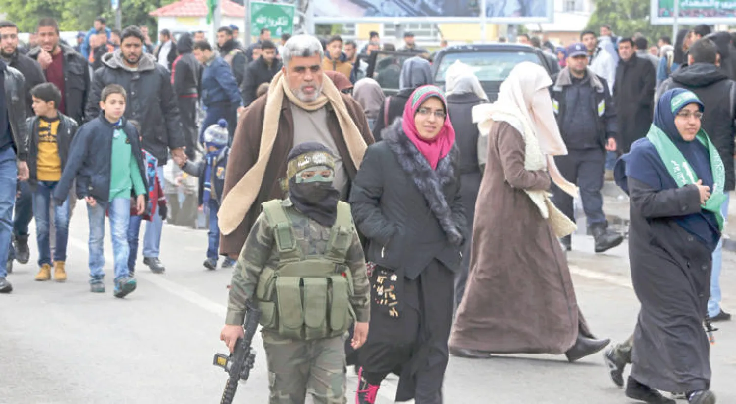 صبي ملثم في زي عسكري يحمل بندقية من البلاستيك دمية في احتفال حماس بذكرى تأسيسها (أ.ب)