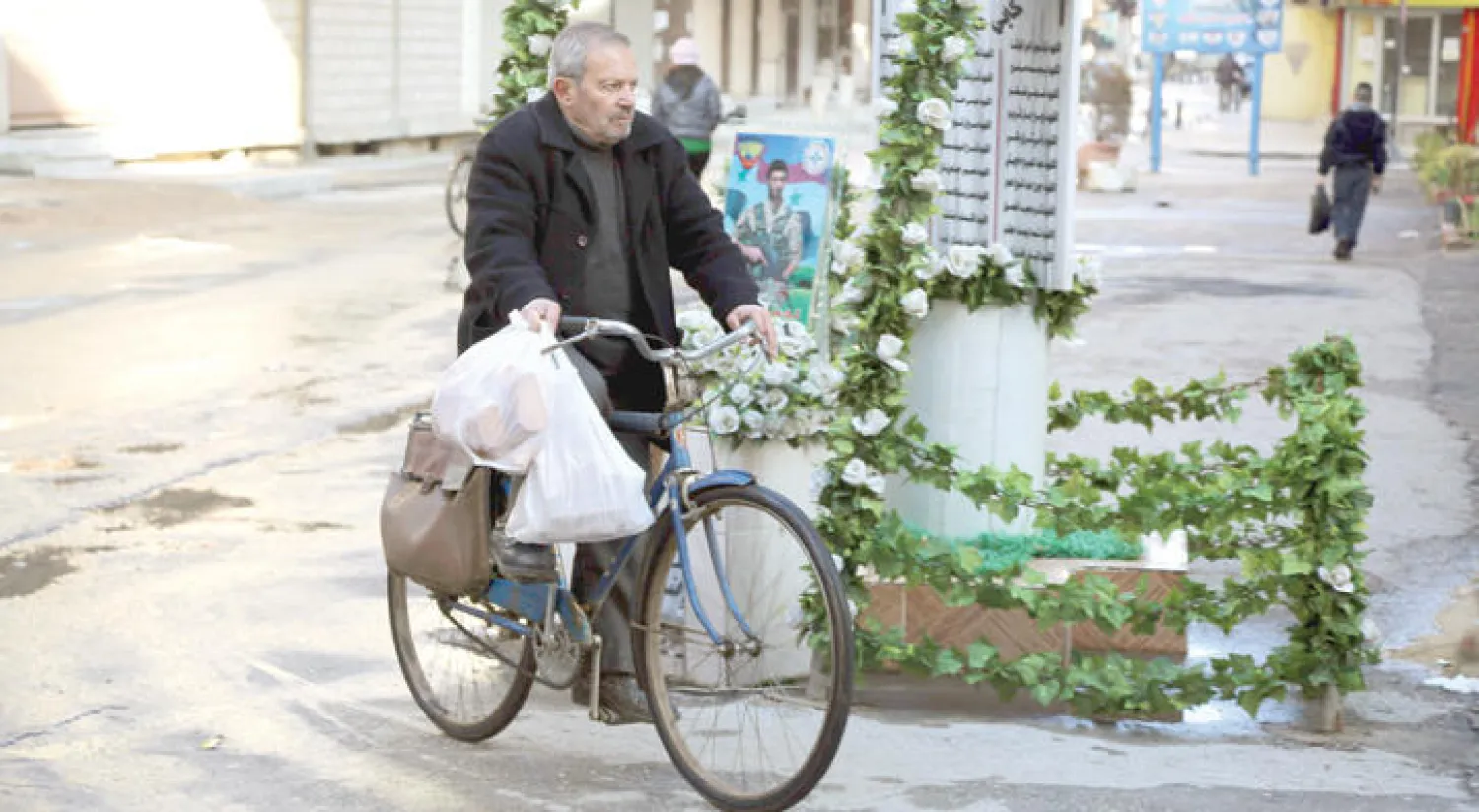 رجل من القامشلي ذات الأغلبية الكردية شمال شرقي سوريا يقود دراجته قرب نصب تذكاري لضحايا مقاتلي مجموعة «سوتورو» المسيحية (أ.ف.ب)