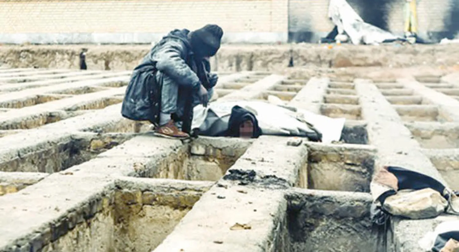 مشرد يفحص قبرًا للمبيت في مقبرة «نصير آباد» بضواحي طهران ({الشرق الأوسط})