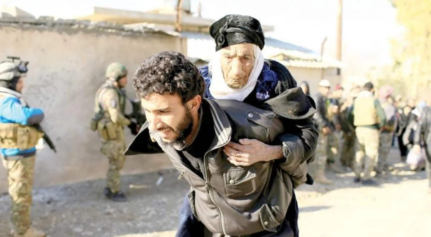 نازح يحمل على ظهره مسنة في حي الميثاق بالجانب الأيسر من الموصل أمس (رويترز)