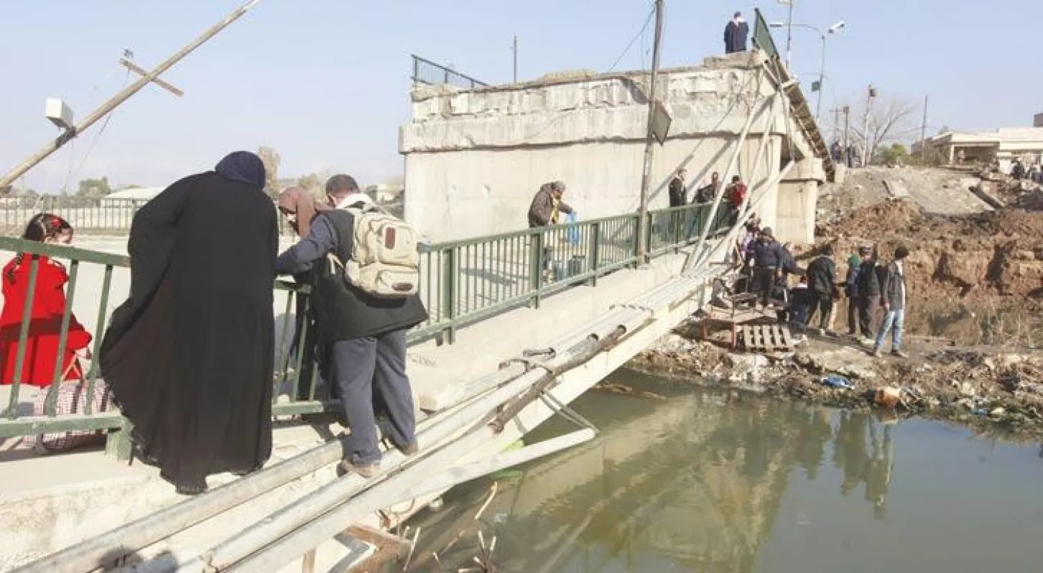 مدنيون يعبرون جسرًا مدمرًا في حي المثنى بالموصل أمس (رويترز)