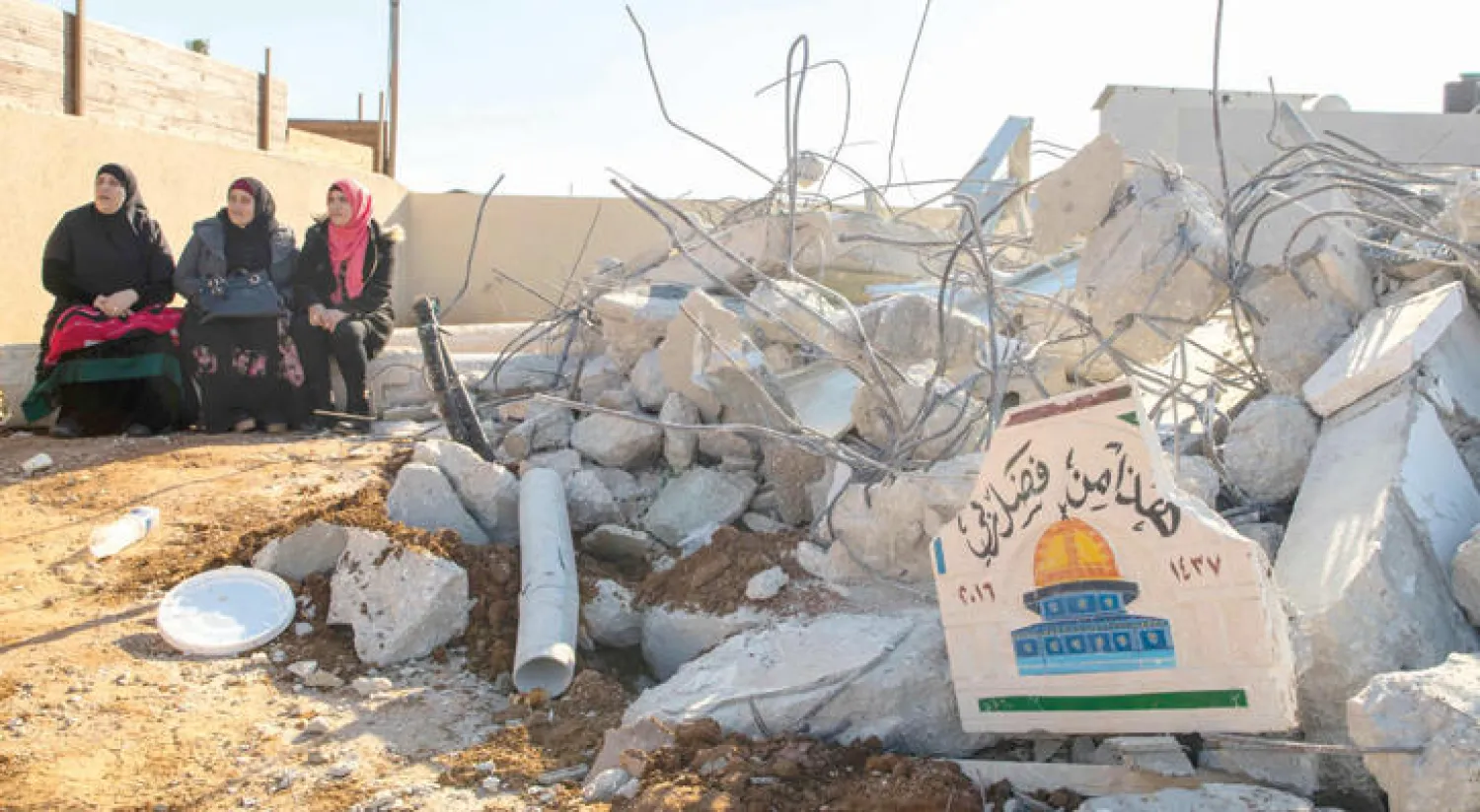 فلسطينيات يجلسن على مقربة من بيت في قلنسوة دمرته السلطات الإسرائيلية بدعوى البناء بلا ترخيص (أ.ف.ب)
