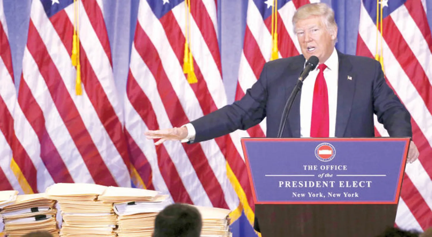 ترامب يتحدث خلال مؤتمر صحافي في نيويوك أمس ويشير إلى مئات الوثائق التي أحضرها لتأكيد ابتعاده عن مجال الأعمال خلال رئاسته (رويترز)