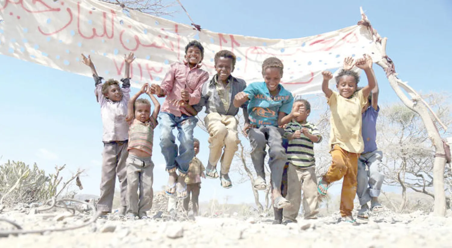 أطفال يلعبون أمام لافته ربطت بين شجرتين وتشير إلى مخيم نازحين في تعز (أ.ف.ب)