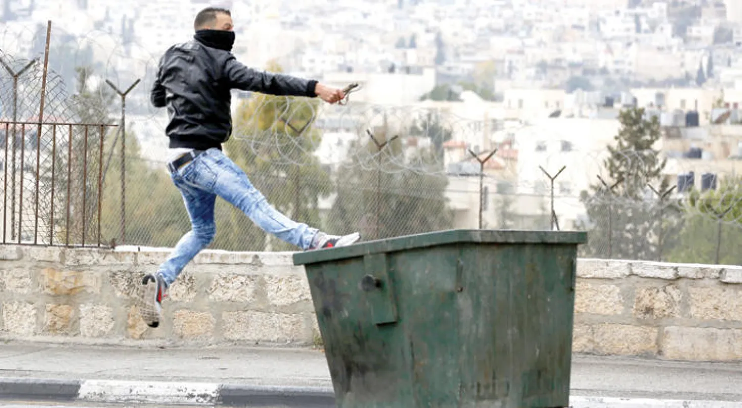 فلسطيني يقذف الحجارة على حاجز للقوات الاسرائيلية خلال احتجاجات على المدخل الشمالي لمدينة الخليل أمس تطالب بإسترداد جثث لفلسطينيين تحتجزها السلطات (إ.ب.أ)