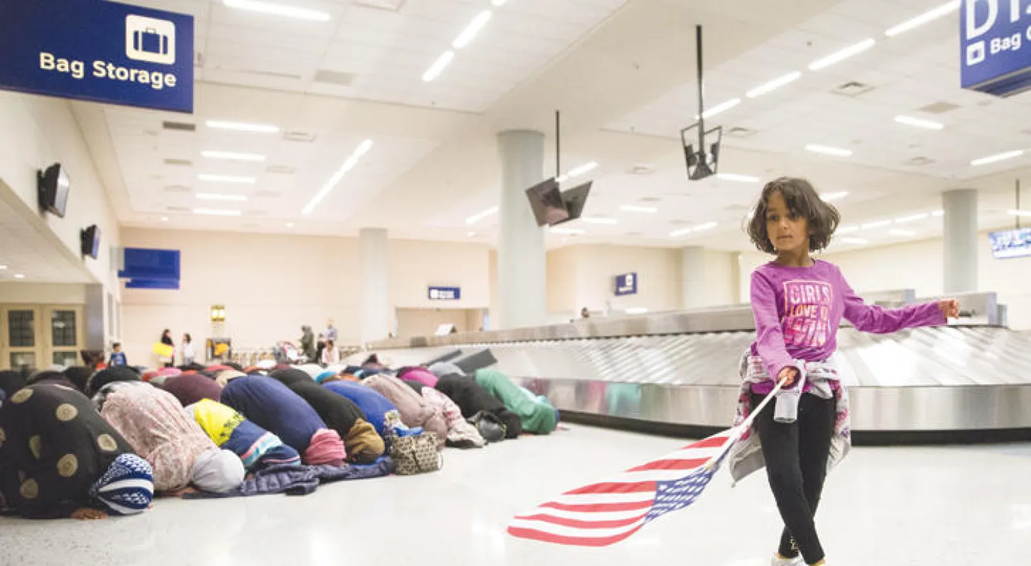 طفلة تحمل علما أميركيا خلال أداء نساء مسلمات الصلاة في مطار دالاس احتجاجا على قرار حظر المسافرين (رويترز)