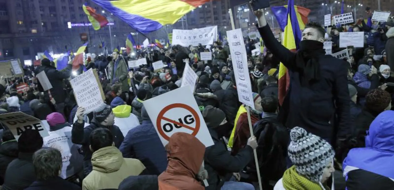 شاب روماني يلتقط صورة بهاتفه الجوال بينما المتظاهرون حوله يغنون النشيد الوطني خلال مظاهرة احتجاج أمام مقر الحكومة في بوخارست (إ.ب.أ)