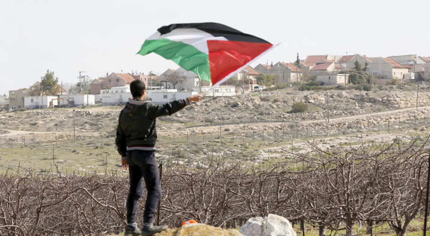 فلسطيني يحمل علم بلاده خلال مظاهرة ضد الاستيطان في بلدة تواني بالضفة الغربية أمس (إ.ب.أ)