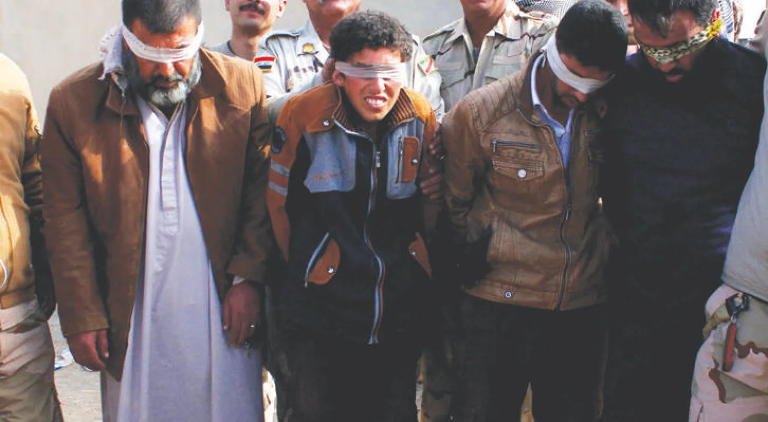 الفتى محمد «قناص داعش» يتوسط والده وعمه أثناء اقتيادهم إلى التحقيق («الشرق الأوسط»)