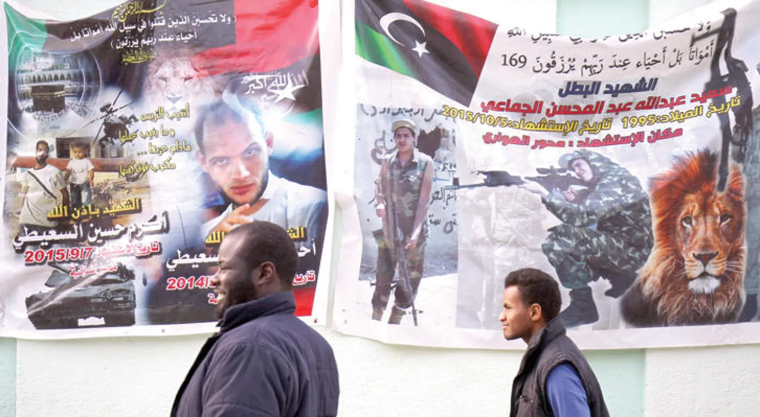 ليبيان يمران بالقرب من ملصقات في شوارع بنغازي تحمل صور مواطنين قتلوا بسبب المعارك الطاحنة في البلاد (أ.ف.ب)