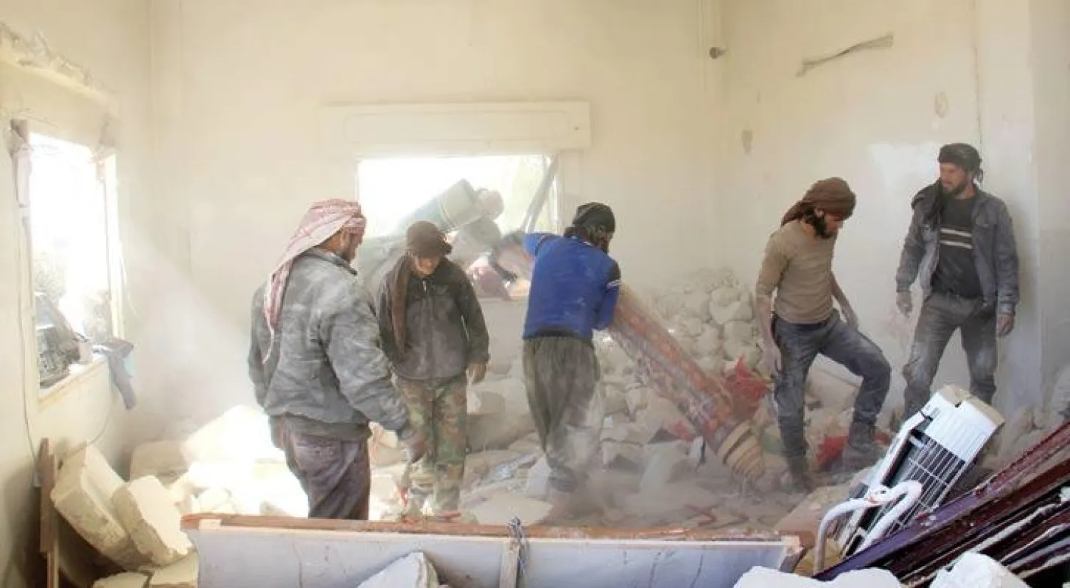 فريق من «الدفاع المدني» يتفقد منزل الطفل عبد الباسط الصطوف الذي بترت ساقاه بقصف لقوات النظام السوري على بلدته الهبيط بمحافظة إدلب قبل 3 أيام (أ.ف.ب)