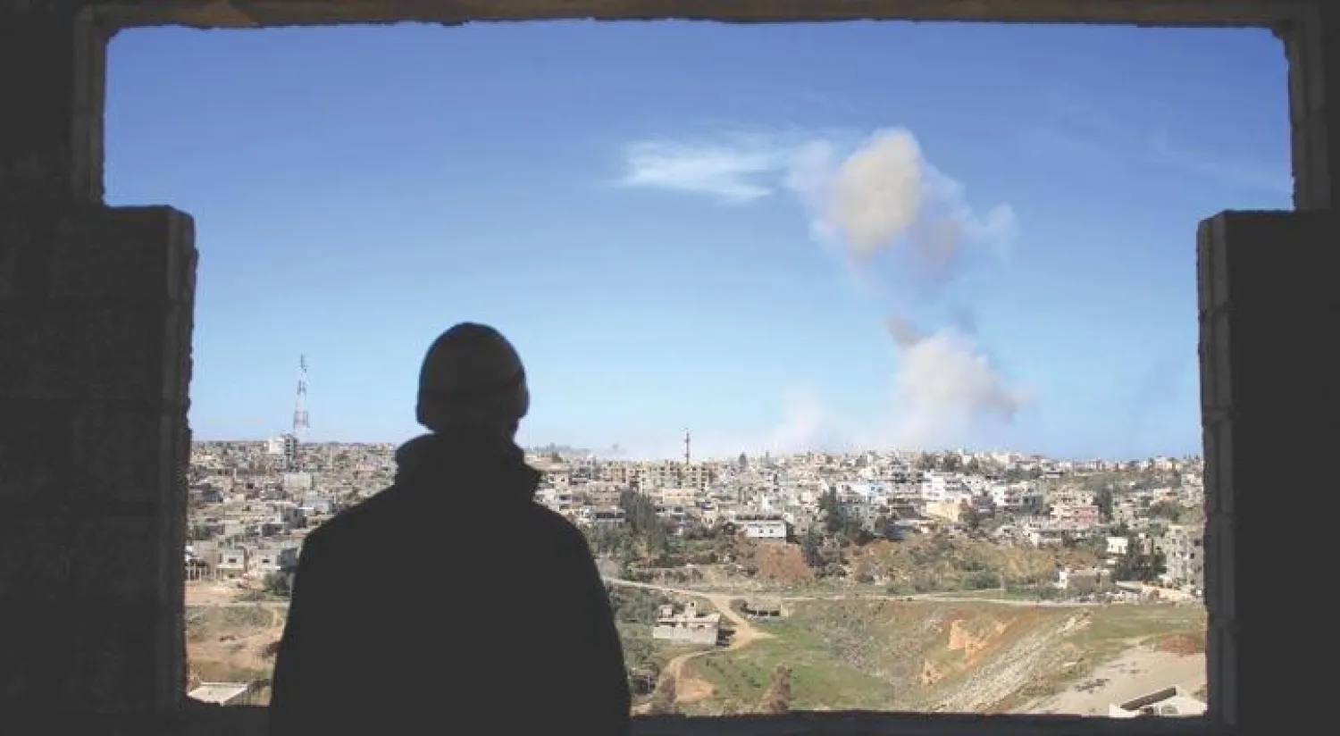رجل من درعا جنوب سوريا، يرقب الدخان المتصاعد من معارك في المدينة وما حولها، بين قوات النظام وفصائل معارضة للسيطرة على المنطقة (أ.ف.ب)