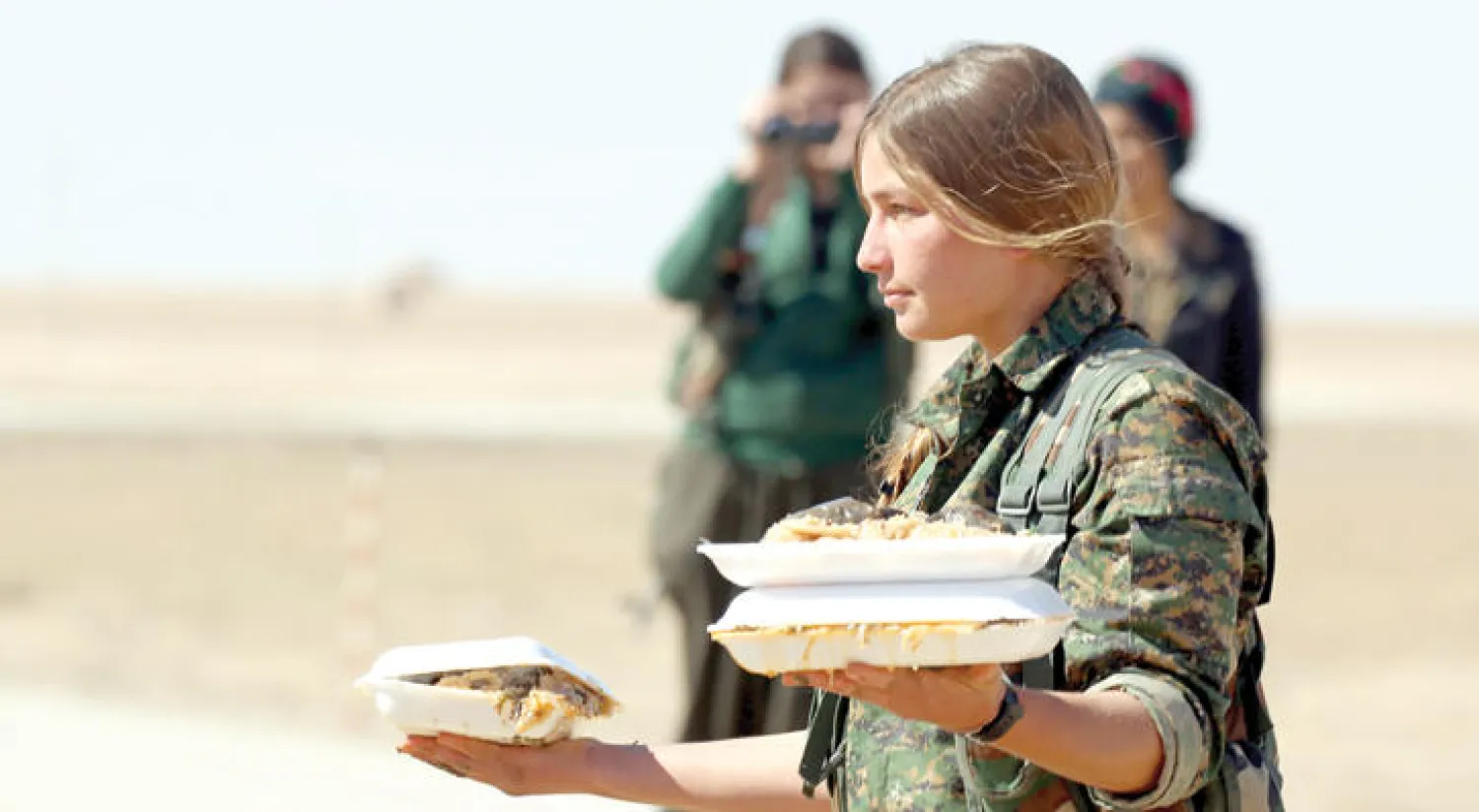 مقاتلة كردية من «قوات سوريا الديمقراطية» توزع وجبات طعام في قرية «صباح الخير» قرب مدينة دير الزور شرق سوريا بعد تقدمها ضد «داعش» بالمنطقة (أ.ف.ب)