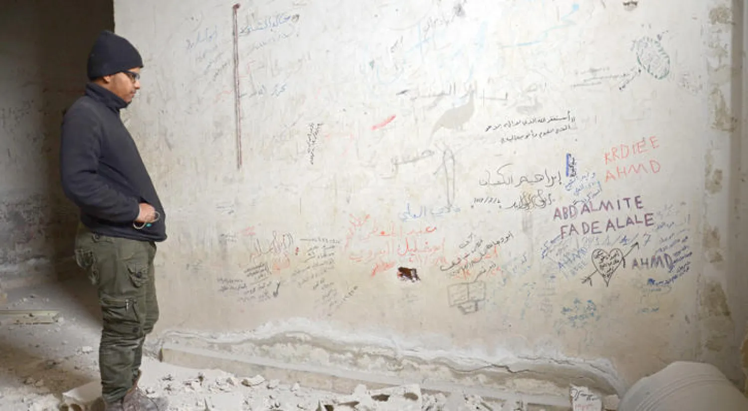 خليفة الخضر معتقل سابق لدى «داعش» في مدينة الباب يقف قرب جدار داخل سجن كان ورفاقه يكتبون عليه ملاحظاتهم (أ.ف.ب)