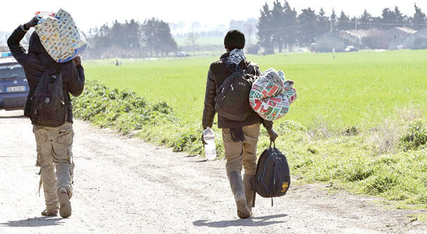 مهاجران غير شرعيين يحملان أغراضهما بعد أن شبت النيران في مخيم بجنوب إيطاليا (رويترز)