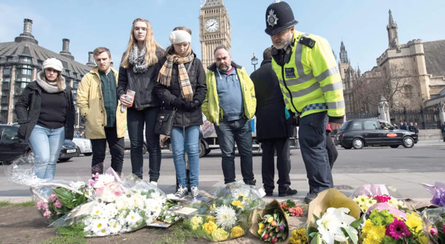 ضابط شرطة من {اسكوتلنديارد} ومارة ينظرون إلى أكاليل الورود في موقع الهجوم على البرلمان البريطاني أمس