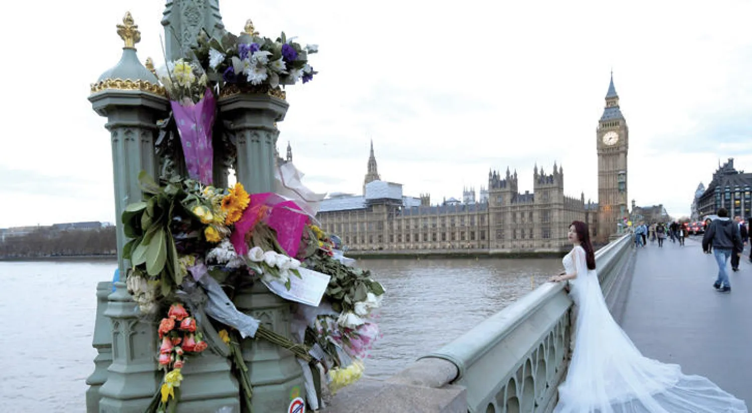 عروس بريطانية على جسر وستمنستر بالقرب من باقات ورود وضعت بعد الحادث الإرهابي على البرلمان البريطاني الأربعاء قبل الماضي وخلّف أربعة قتلى و50 جريحاً على الأقل (رويترز)