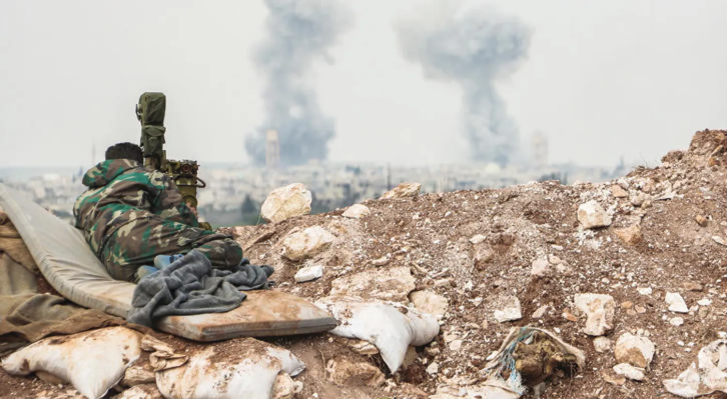 عنصر من قوات النظام يرقب من خلال منظار الدخان المتصاعد من قرية قمحانة بريف حماة إثر قصف من الطيران الحربي أول من أمس (أ.ف.ب)