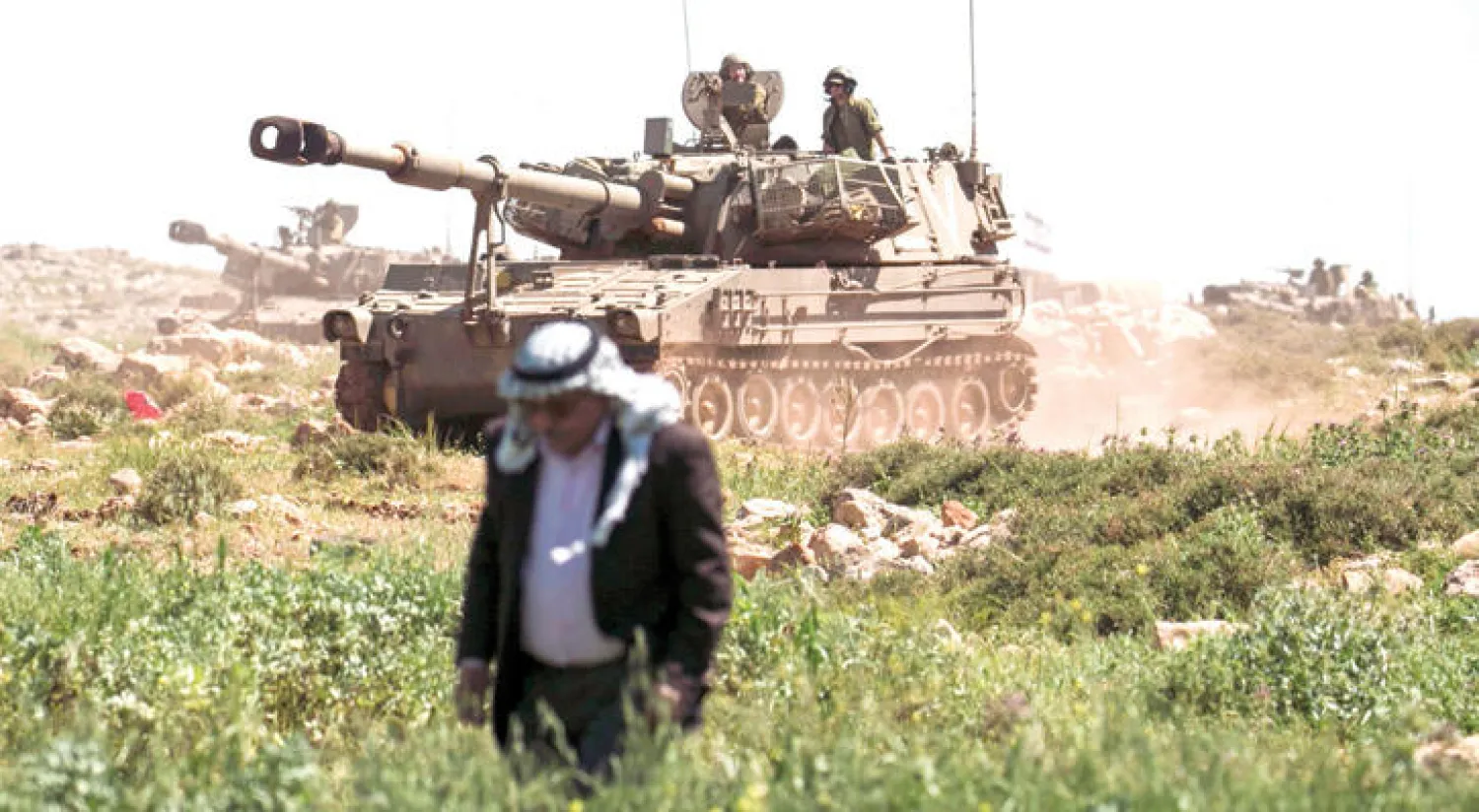 إسرائيليون على ظهر دبابة تمر بالقرب من فلاح فلسطيني خلال تدريبات عسكرية في قرية عقربة (أ.ف.ب)