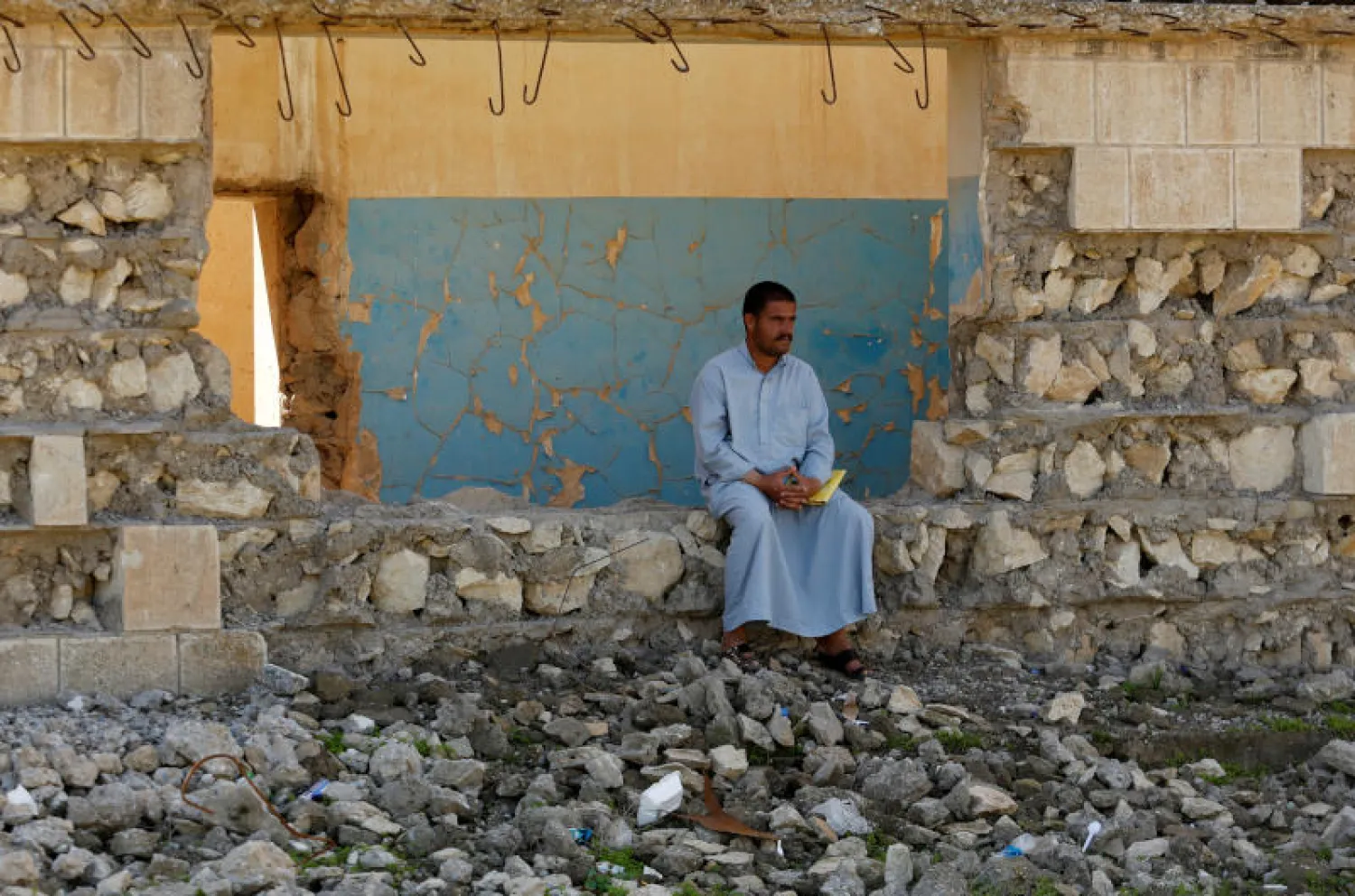 عراقي نازح هرب من منزله يجلس أمام مبنى مهدوم خارج مخيم حمام العليل جنوب الموصل (رويترز)