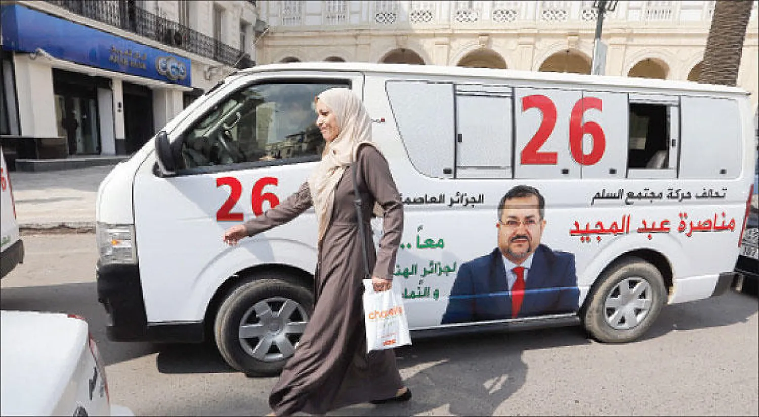 جزائرية تمر بالقرب من سيارة تحمل الشعار الانتخابي لتحالف «حركة مجتمع السلم» أمس (إ.ب.أ)