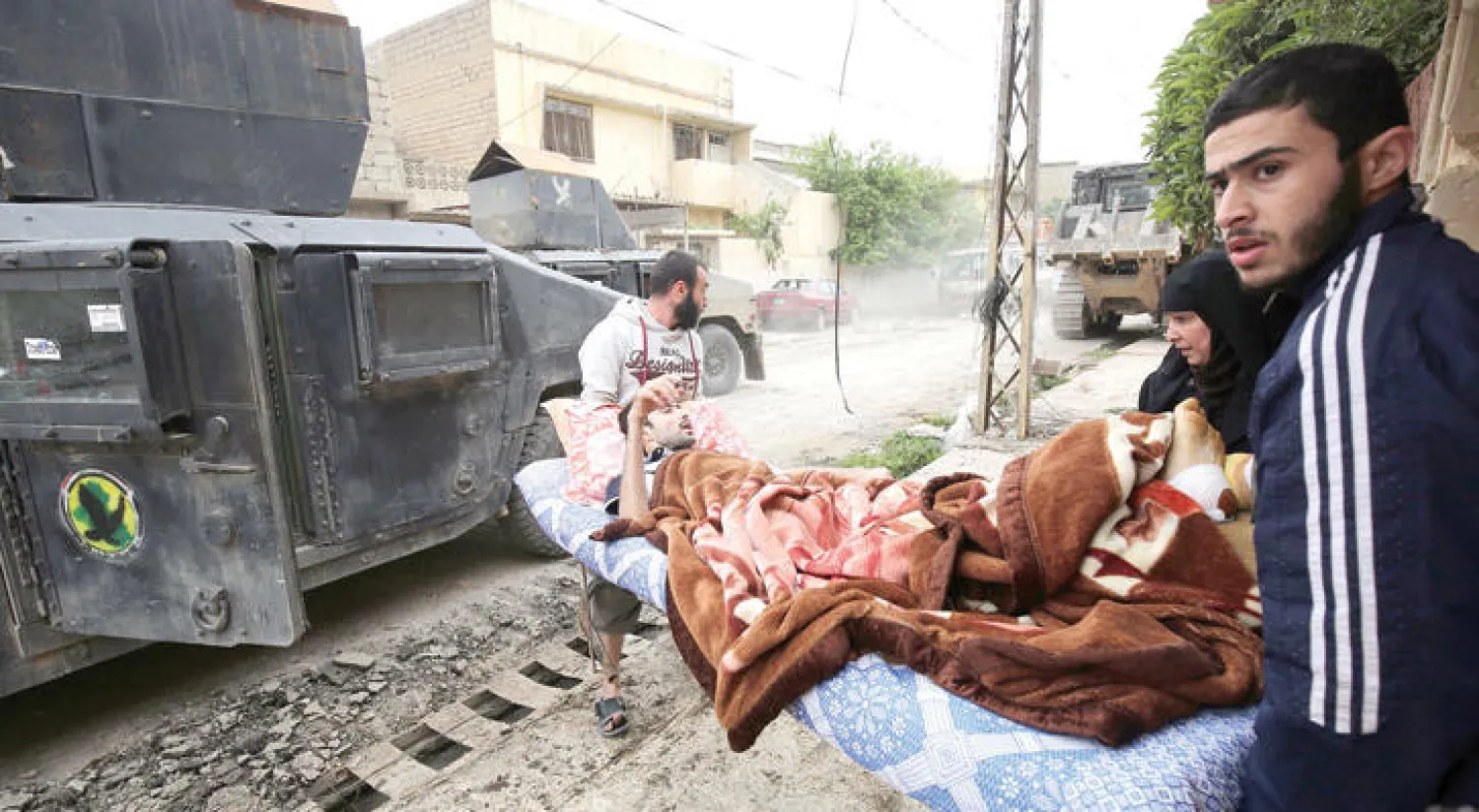 عراقيون ينقلون مريضاً خلال فرارهم من المعارك في حي الآبار غرب الموصل أمس (أ.ف.ب)