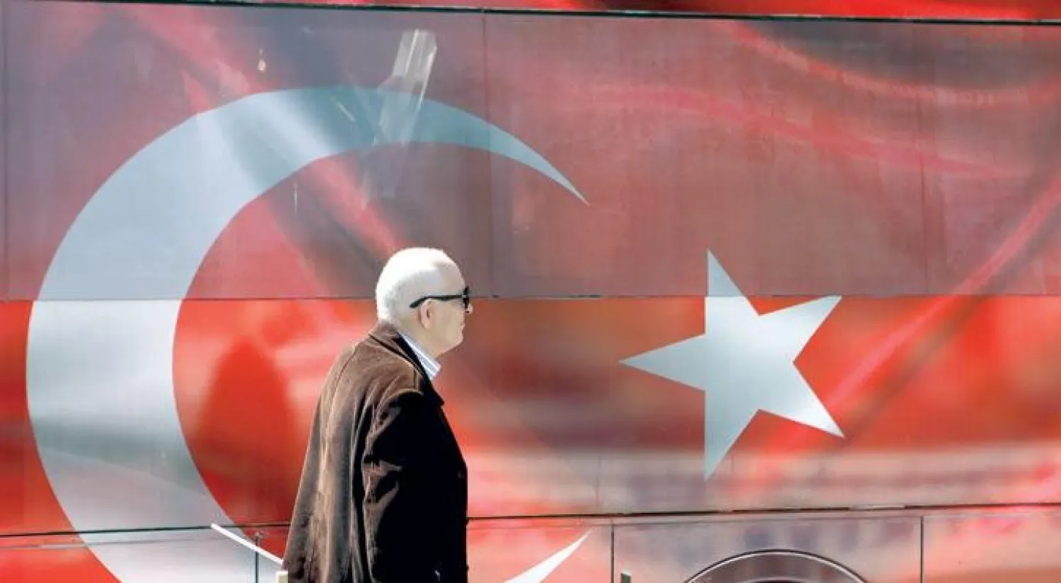 تركي يمر بجانب حافلة والعلم التركي يغطيها في اطار الحملات الداعمة والرافضة للاستفتاء التركي (أ.ب)