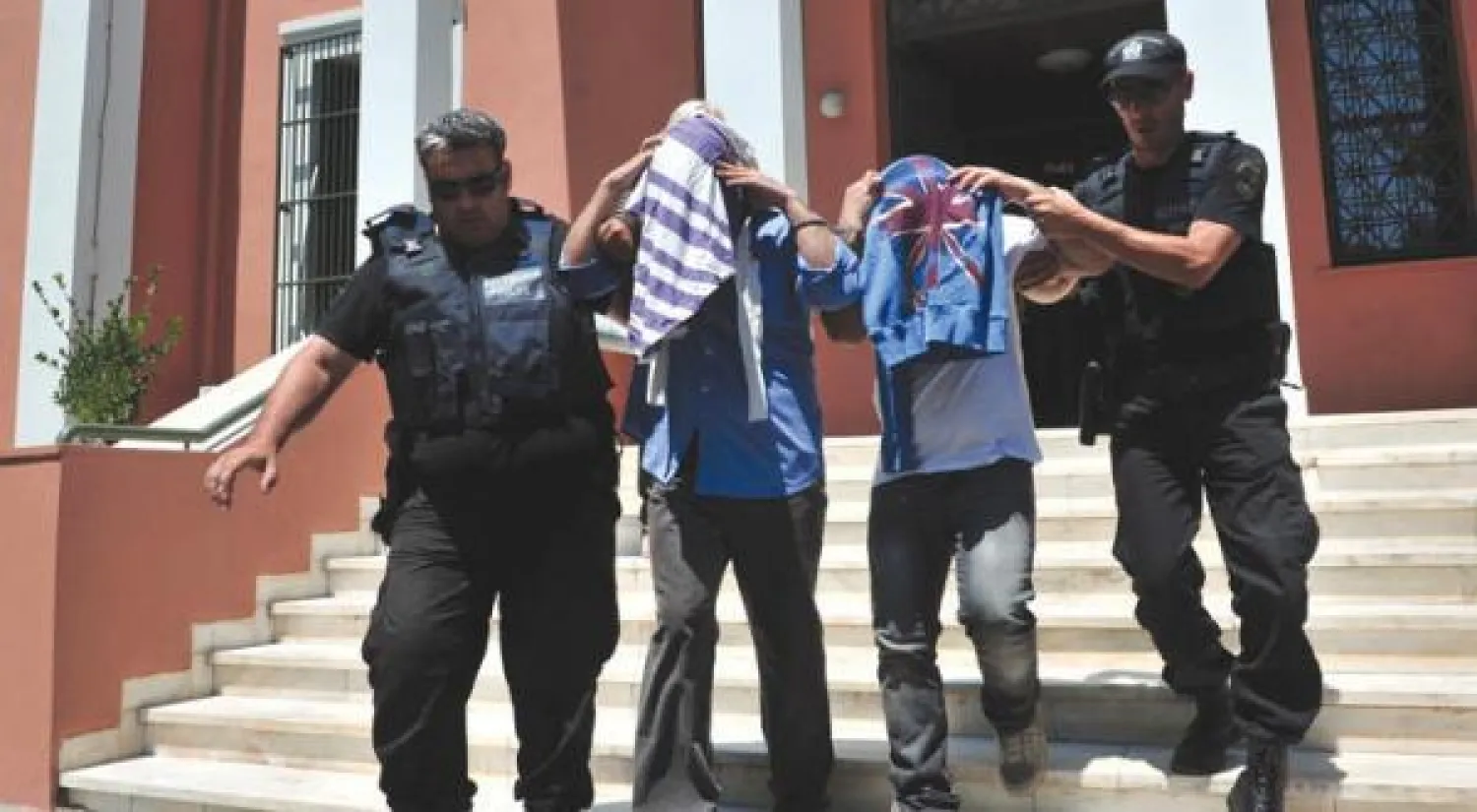 اثنان من أصل ثمانية من الضباط الأتراك الذين فروا إلى اليونان بطائرة هليكوبتر يغادران مبنى محكمة ألكساندروبولي مرفوقين برجلي شرطة يونانيين (أ.ف.ب)