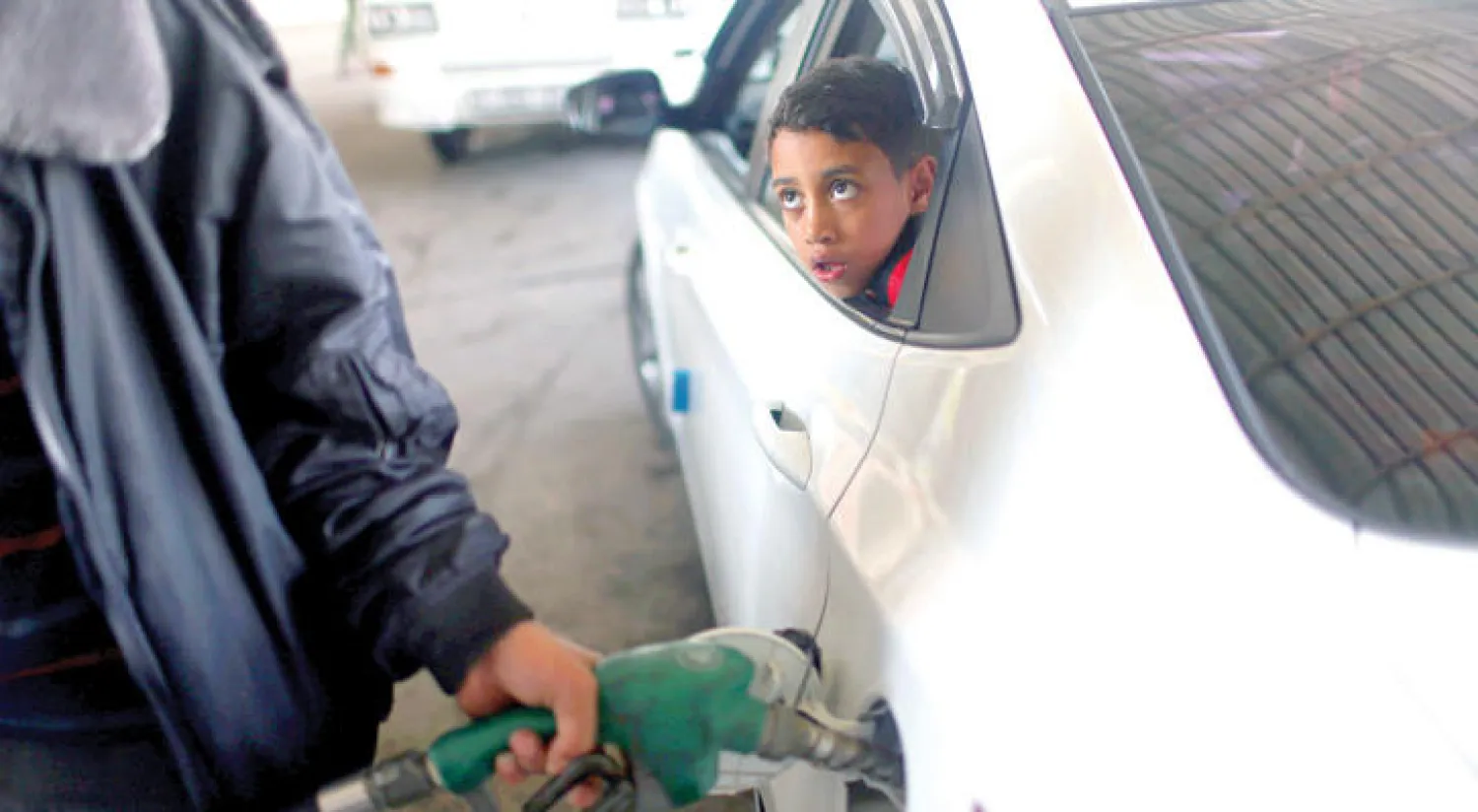 طفل فلسطين يتابع داخل سيارة عامل محطة بنزين يملأ خزانها (رويترز)
