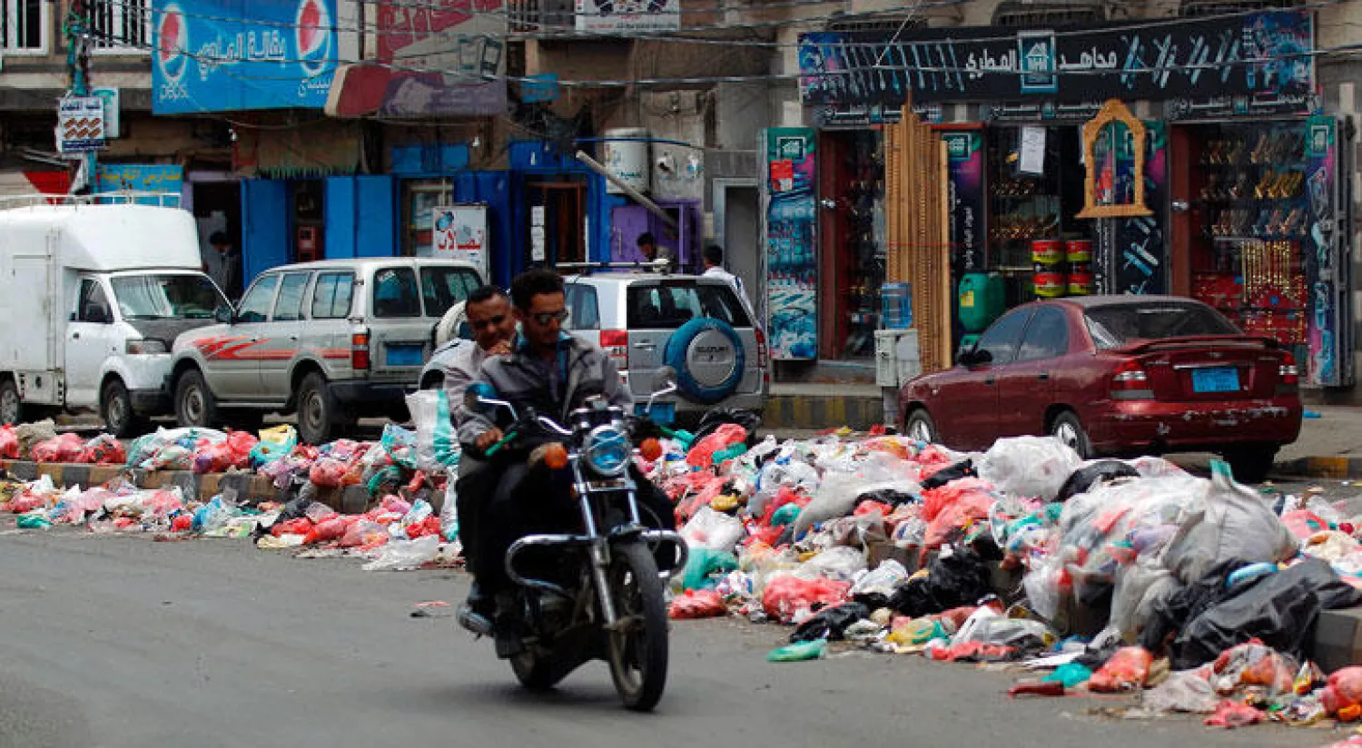 يمنيان على متن دراجة نارية قرب أكوام من القمامة في العاصمة صنعاء أمس (أ.ف.ب)