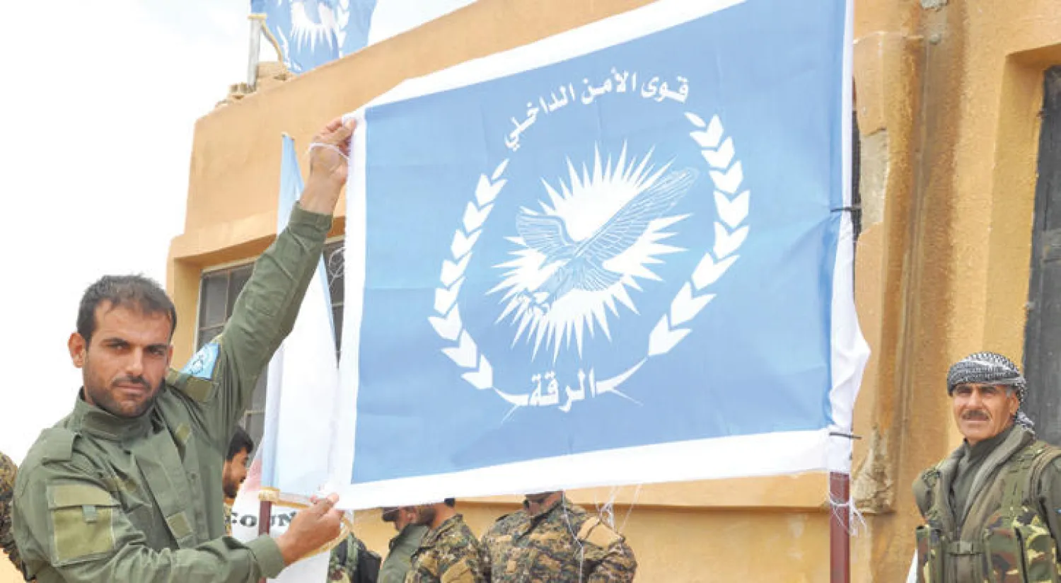 متدرب من قوات الأمن الداخلي في عين عيسى يرفع علم القوات وهي أول شرطة يشكلها التحالف الدولي في محافظة الرقة (أ.ف.ب)