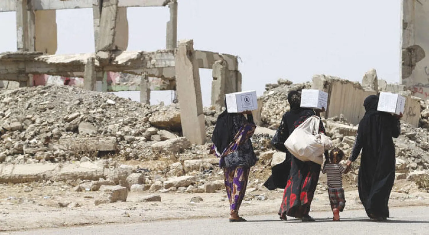 نازحات عراقيات يمررن قرب مبانٍ مهدمة جنوبي الموصل أمس (أ.ف.ب)