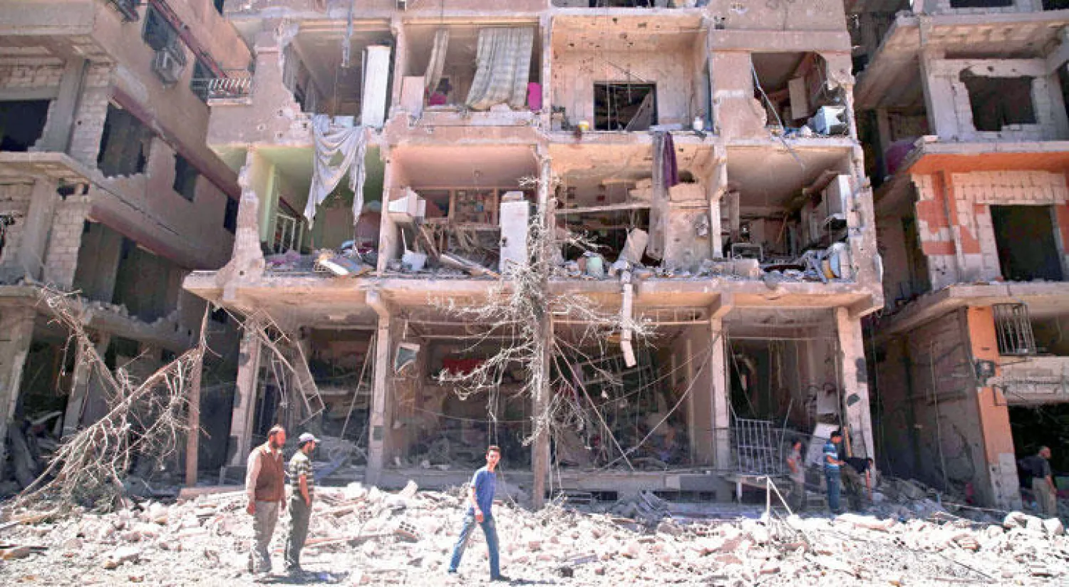 سوريون من عين ترما في غوطة دمشق يعبرون أمام بناء مدمر (أ. ف. ب)