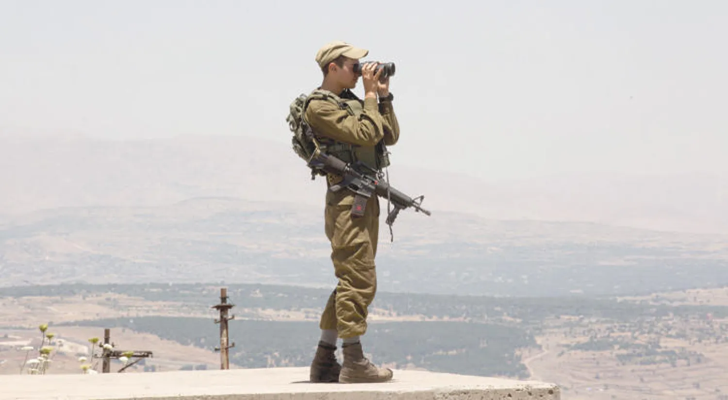 جندي إسرائيلي فوق هضبة الجولان المحتلة يراقب دخان معارك في القنيطرة السورية القريبة (إ.ب.أ)