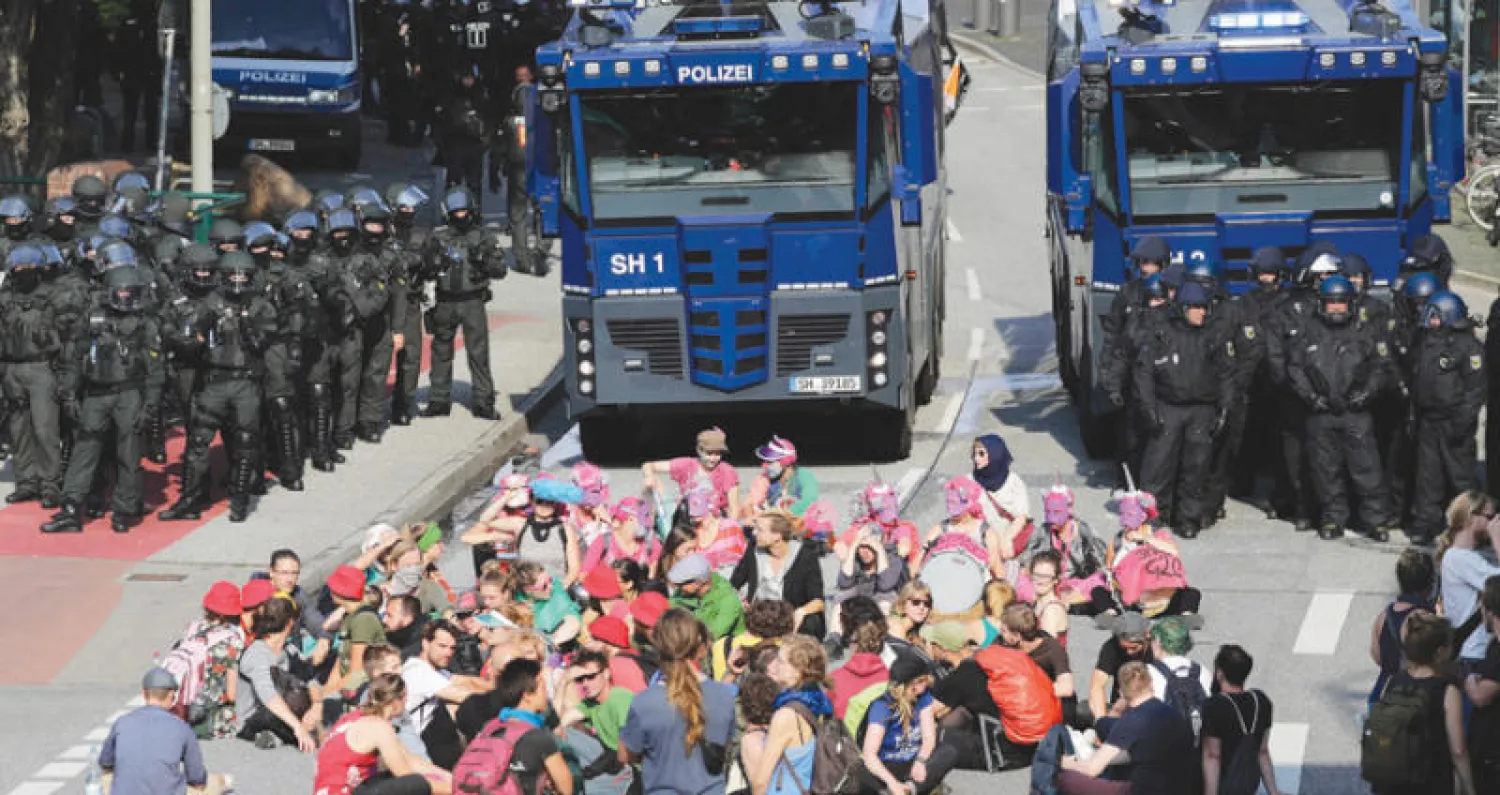 محتجون يفترشون الأرض أمام سيارات خراطيم المياه التي استخدمتها الشرطة لتفريقهم (إ.ب.أ)