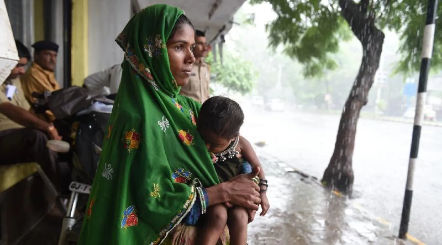 امرأة هندية تحمل طفلها بانتظار توقف الأمطار (أ.ف.ب)