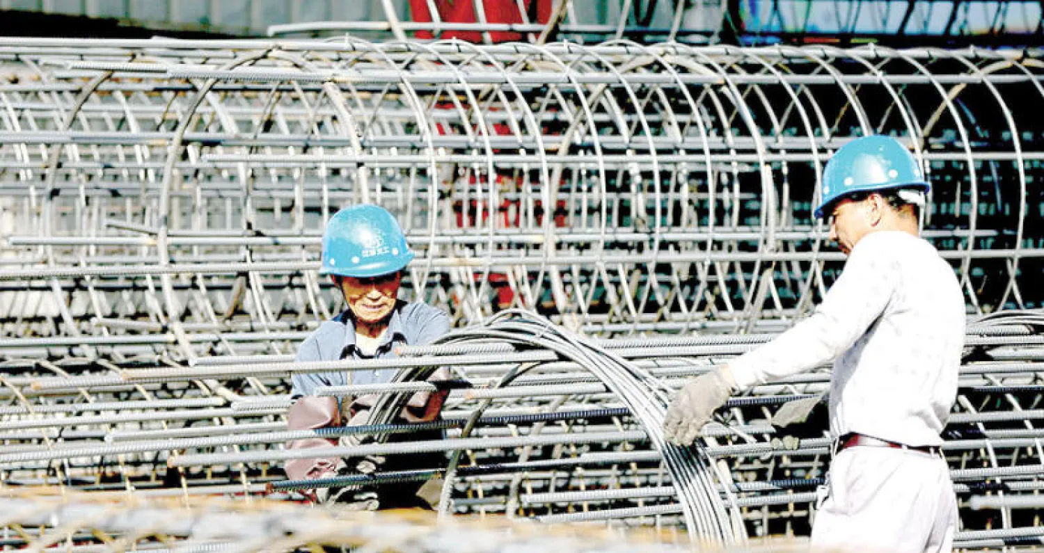 عاملان صينيان يعملان على صنع أقفاص فولاذية لأساسيات البناء في موقع بناء بمحافظة جيانغسو الصينية (رويترز)