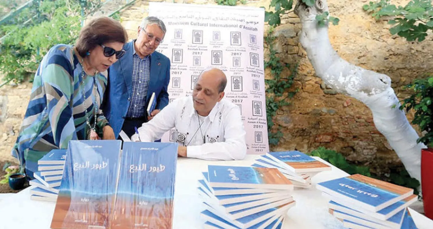 ولد محمدي يوقع روايته «طيور النبع» لبهية الجشي سفيرة مملكة البحرين ويبدو في الوسط محمد بن عيسى أمين عام مؤسسة منتدى أصيلة