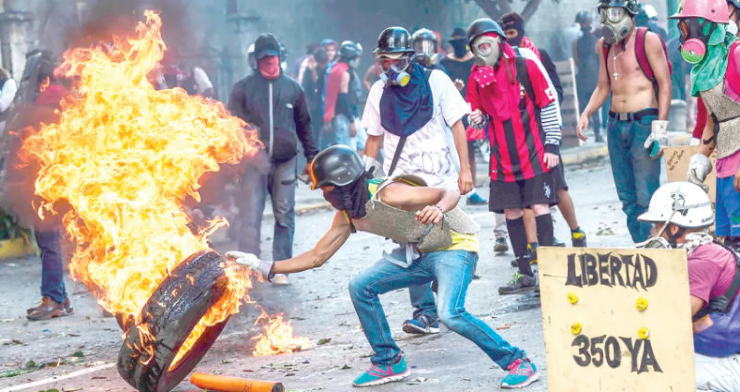 متظاهرون فنزويليون يحرقون إطار سيارة للتعبير عن رفضهم لسياسات حكومة مادورو في كاراكاس أمس (أ.ف.ب)