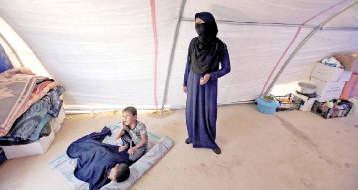 امرأة مع طفليها في أحد المخيمات جنوب الموصل (رويترز)