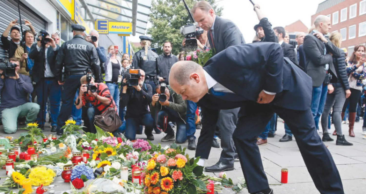 عمدة هامبورغ أولف شولتز ووزير داخليتها أندي غروته يضعان أكاليل من الورود على أرواح الضحايا  أمام مدخل المتجر الذي شهد اعتداء الطعن أول من امس (إ.ب.أ)