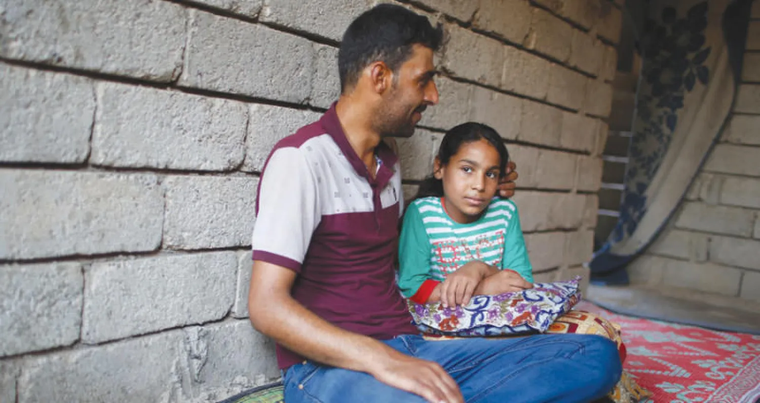 طفلة عراقية تجلس بجوار والدها في منزلهما في شرق الموصل بعد أن فرقتهما المعارك (رويترز)