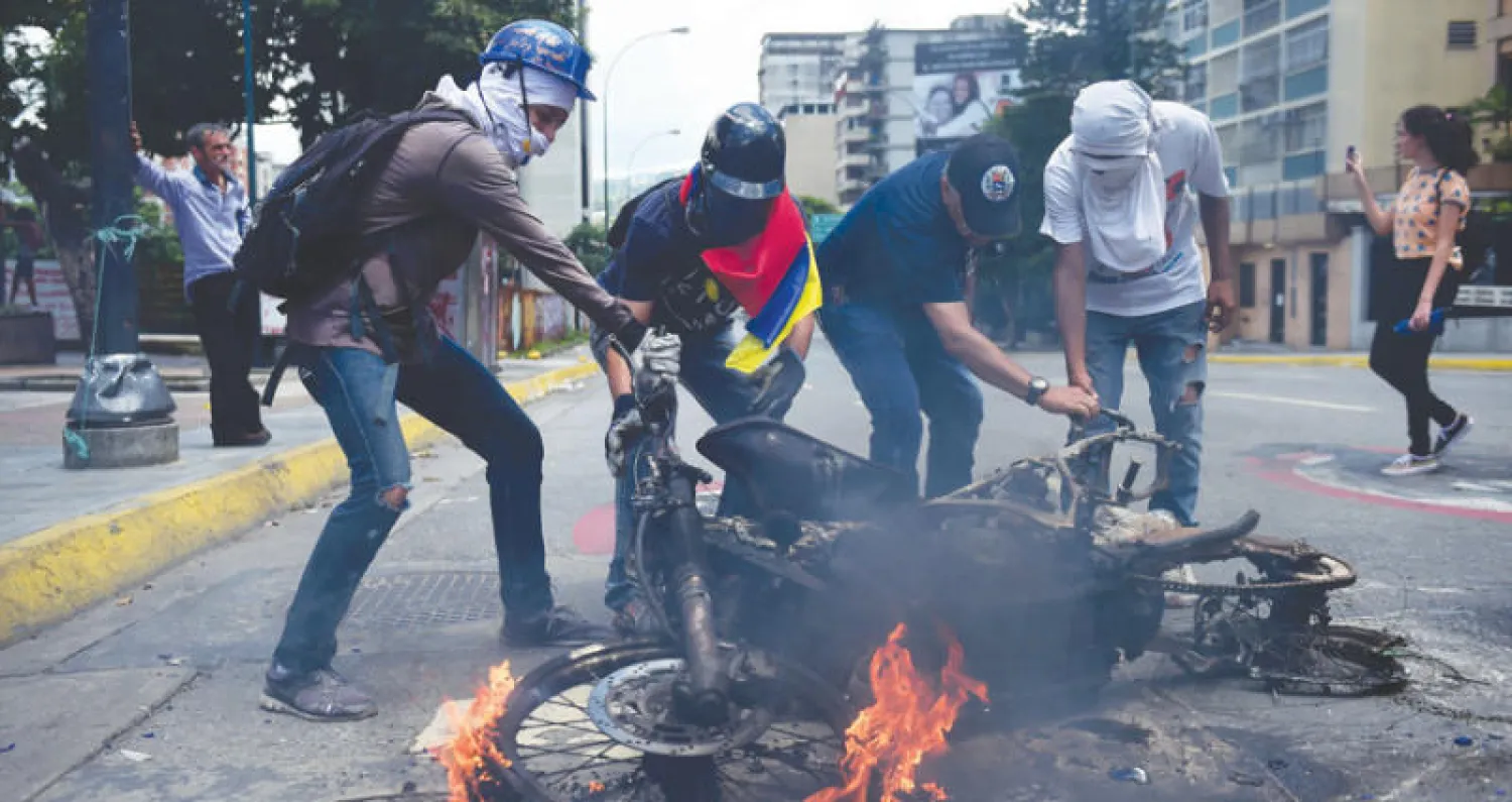 معارضون فنزويليون يزيحون دراجة نارية تابعة للشرطة بعد انفجار في كاراكاس أمس (أ.ف.ب)